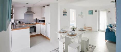 A modern kitchen with white cabinetry, a dining area with a white table, and a blue sofa in the living room.