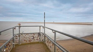 Una escalera metálica conduce a una playa con una valla decorada con numerosos candados.
