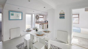 Una cocina moderna con armarios blancos, una mesa de comedor preparada para cuatro personas y vistas al dormitorio contiguo.