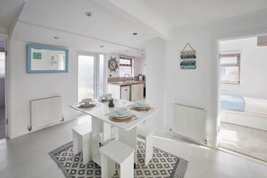 A modern kitchen with white cabinetry, a dining table set for four, and a view into the adjacent bedroom.