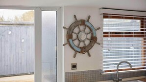 Una cocina con ventana, un lavamanos y un adorno de timón colgado en la pared.