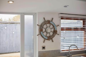 A kitchen with a window, a sink, and a wall-mounted ship's wheel decoration.