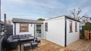 Un patio con sofá y mesa, una terraza de madera y un edificio blanco con ventanas.