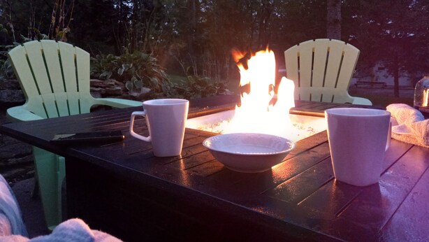 A table with two chairs, a bowl, and two mugs, with a fire burning in the background. - Beach Garden Bungalow - Relax Near The River (Poynette)