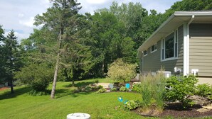 A residential property with a well-maintained lawn, a variety of trees, and a house with a light-colored exterior. - Beach Garden Bungalow - Relax Near The River (Poynette)