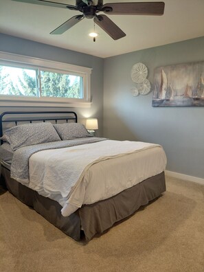 A bedroom with a bed, a ceiling fan, a window, and a wall painting. - Start your Summer with a Vaca at the Beach Garden Bungalow (Poynette)