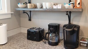 A kitchen with a 'WELCOME TO OUR COTTAGE' sign, a toaster, a coffee maker, and various mugs and bowls on shelves. - Beach Garden Bungalow - Relax Near The River (Poynette)