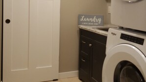 A laundry room with a closed door, a sign that says "Laundry," and a stacked washer and dryer. - Beach Garden Bungalow - Relax Near The River (Poynette)