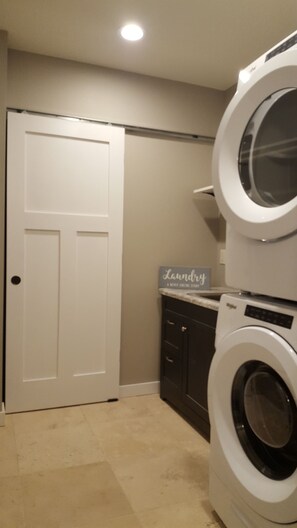 Ein Waschraum mit geschlossener Tür, einem Schild mit der Aufschrift 'Laundry' und einer gestapelten Waschmaschine und einem Trockner.