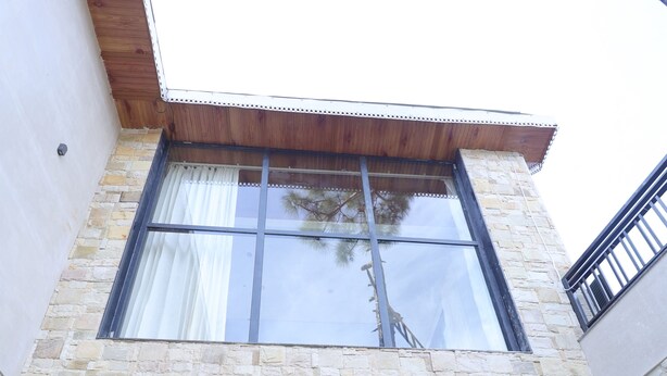 A modern building with stone facade, large glass doors, and a wooden overhang. - MINARA MEADOWS (Kasauli)