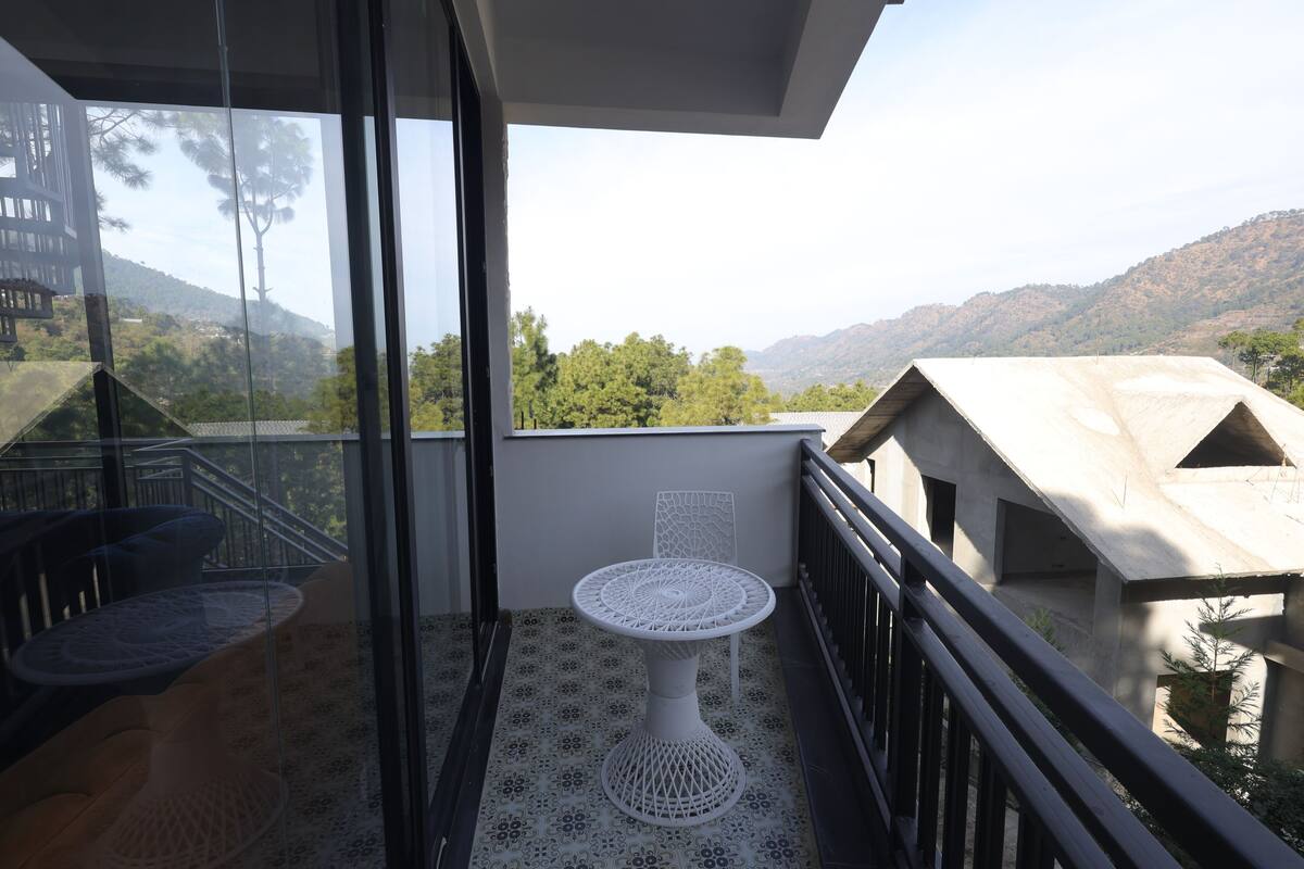 Uma varanda com mesa e cadeira brancas, uma porta de vidro e vista para uma paisagem montanhosa.