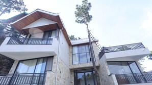 A multi-story building with stone facade, balconies with metal railings, and large windows. - MINARA MEADOWS (Kasauli)