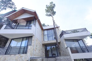 A multi-story building with stone facade, balconies with metal railings, and large windows. - MINARA MEADOWS (Kasauli)