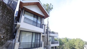 A multi-story building with balconies, stone walls, and a view of trees. - MINARA MEADOWS (Kasauli)