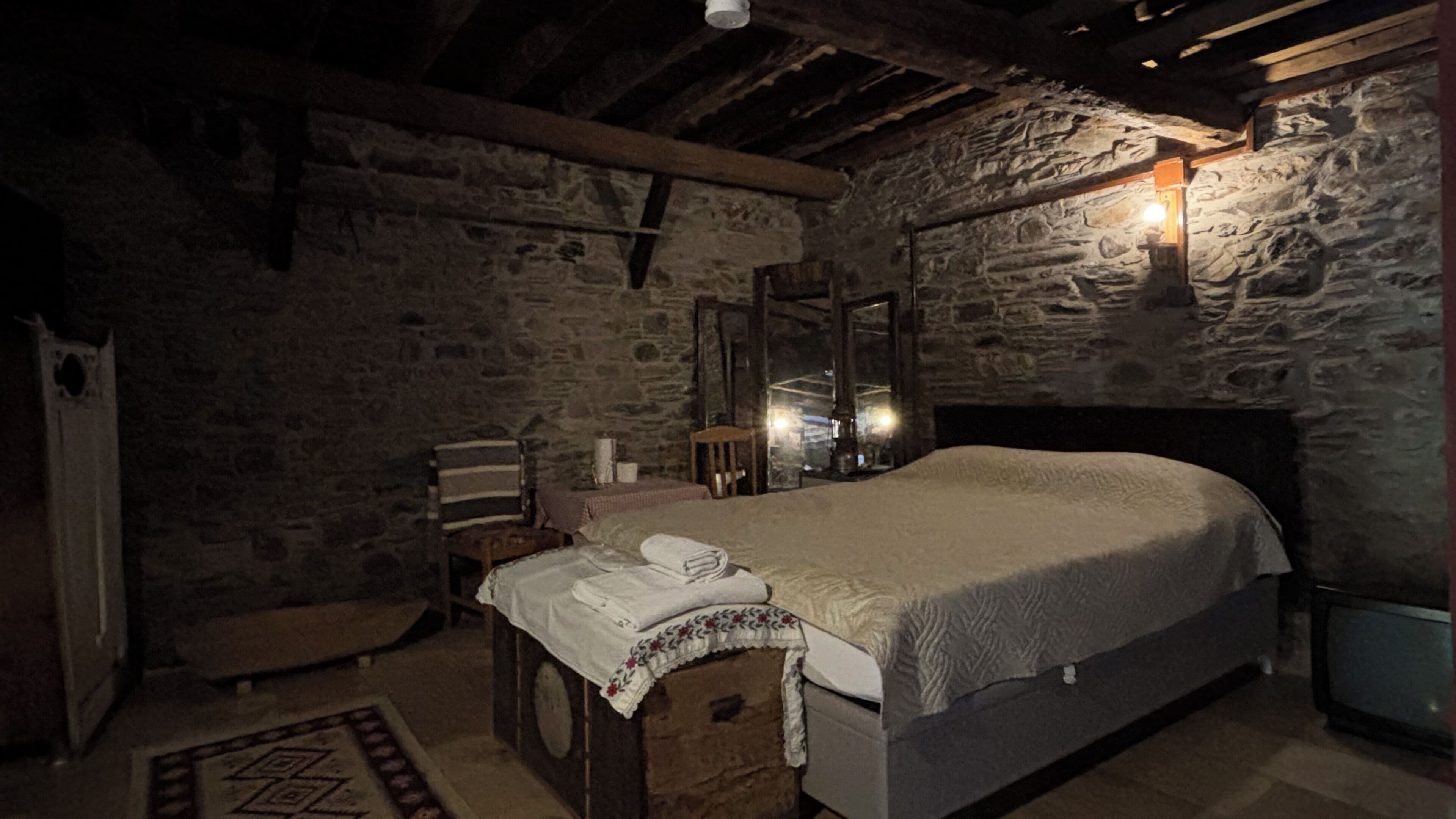 Ein Zimmer mit Stehwänden, einem Bett, einem Sessel, einem Tisch und einem Spiegel.