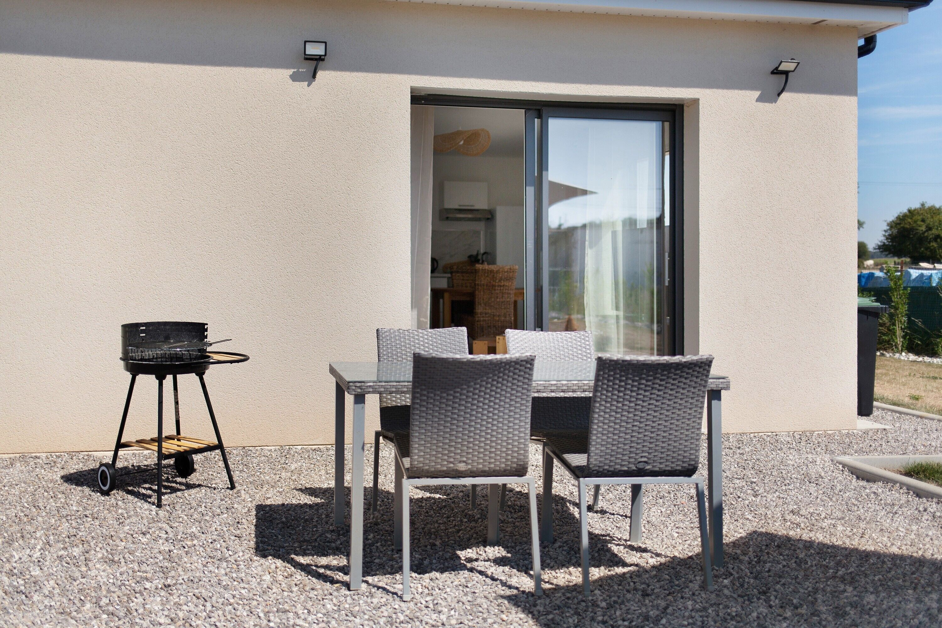 Un patio al aire libre con una mesa, sillas, una parrilla y una puerta corrediza de vidrio que da a un espacio interior.