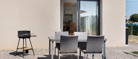 An outdoor patio with a table and chairs, a grill, and a sliding glass door leading to an interior space.