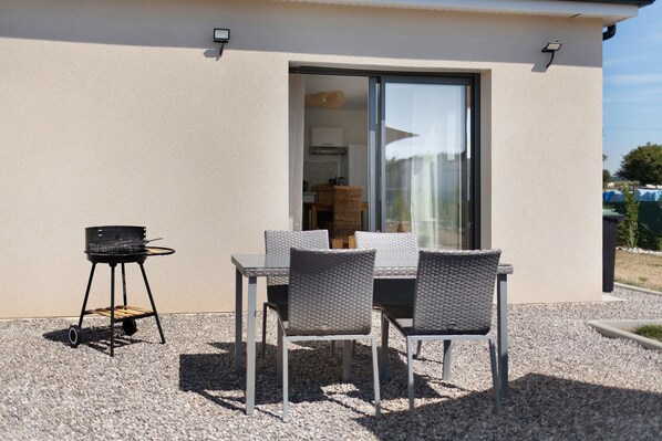 Une terrasse extérieure avec une table et des chaises, un barbecue et une porte-fenêtre coulissante donnant sur un espace intérieur.