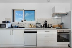 A modern kitchen with white cabinetry, a built-in dishwasher, a stove, and a window with a view of the sky. - Holiday Home 'Maison Sci Entre Foret Et Mer' with Wi-Fi (Millebosc)