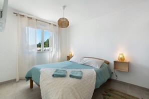 Une chambre à coucher avec un lit, une fenêtre avec des rideaux, un luminaire suspendu et des lampes de chevet.