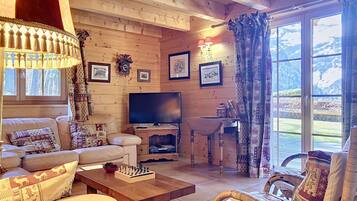 Un salon chaleureux avec un canapé, une table basse en bois, un téléviseur et une vue sur les montagnes grâce à de grandes fenêtres.