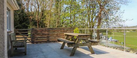 An outdoor patio with a picnic table and benches, surrounded by a wooden fence and trees.