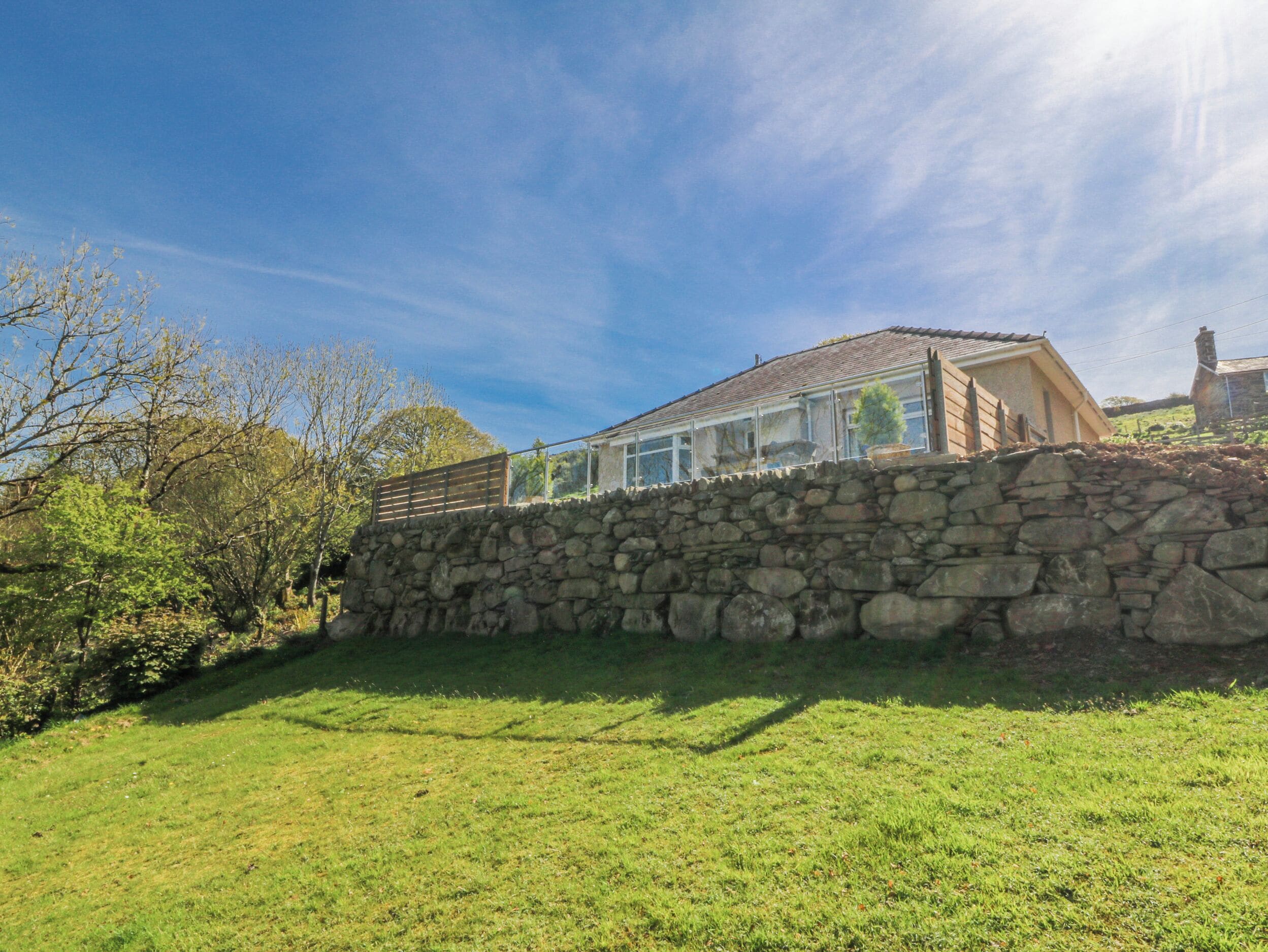 A stone wall with a house behind it, a clear sky, and some trees.