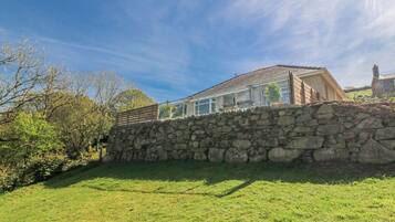A stone wall with a house behind it, a clear sky, and some trees.