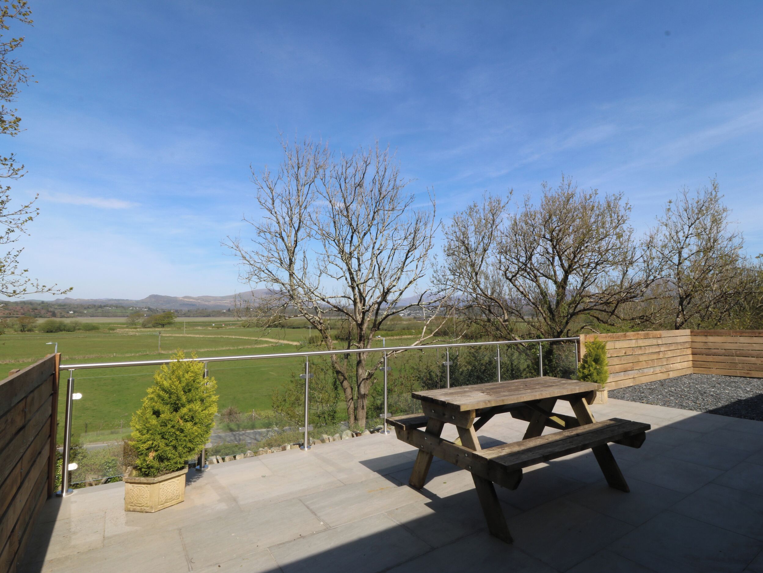 Une terrasse avec une table de pique-nique et un petit jardinière, donnant sur un champ verdoyant et des arbres.