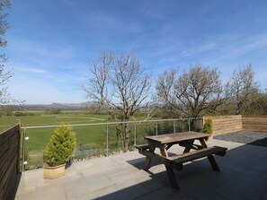 Eine Terrasse mit Picknicktisch und einem kleinen Baumkübel, mit Blick auf ein grünes Feld und Bäume.