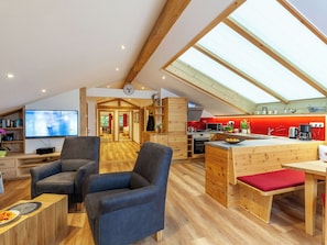 Ein geräumiges Loft mit hoher Decke, Holzbalken, einer Küche mit roten Akzenten und einem großen Fernseher im Wohnbereich.