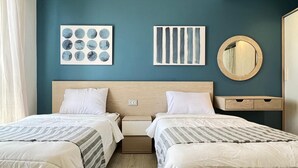 A hotel room with two beds, a wooden headboard, a bedside table, a mirror, and artwork on the wall.