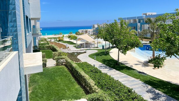 A modern hotel with a pool, a well-maintained lawn, and a view of the ocean.