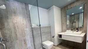 A modern bathroom with a glass shower enclosure, a white toilet, and a vanity with a mirror.