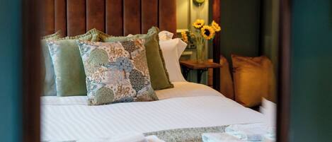 Una habitación de hotel con una cama, almohadas, una mesita de noche, una lámpara y un espejo que refleja la habitación.