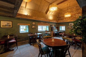 A rustic dining area with wooden tables and chairs, stone walls, and a large plant.