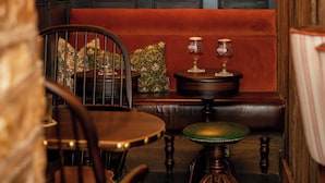 A cozy interior with a red cushioned bench, wooden chairs, a small table with glasses, and framed pictures on the wall.