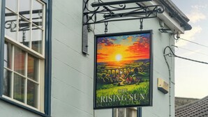 A building with a sign reading 'The Rising Sun' and a window with a view of a sunset.