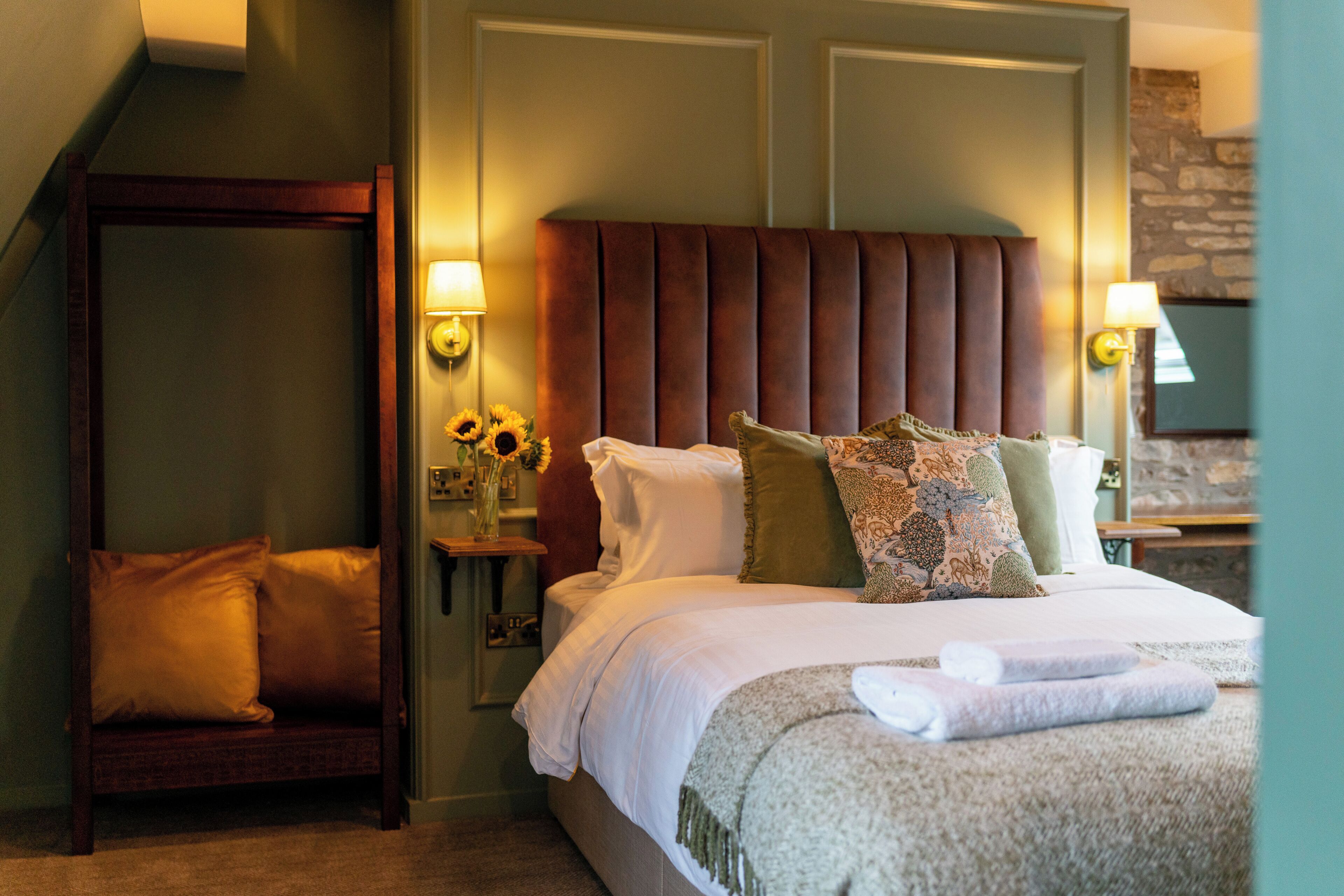 A bedroom with a large bed, a wooden bench, a nightstand with a lamp, and a wall-mounted TV.