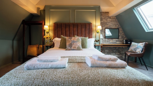 A bedroom with a bed, pillows, a nightstand, a chair, a desk, and a window.