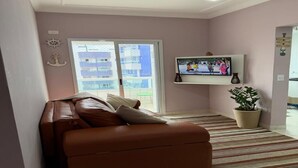 Ein Wohnzimmer mit braunem Ledersofa, einem Fernseher, einer Zimmerpflanze und Blick durch eine Glastür.