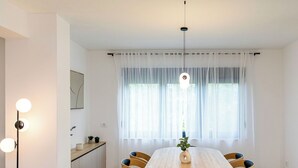 A dining area with a round table, six chairs, a hanging light fixture, a window with sheer curtains, and a small plant on the table. - Stunning private villa for 8 guests with A/C, WIFI, private pool, TV, terrace and pets allowed (Senj)