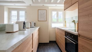 A modern kitchen with wooden cabinets, a marble countertop, a built-in oven, and a window with a view. - Heart Marais Bright 1BR by Melvane (Paris)