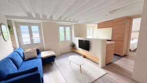 A modern living room with a blue sofa, a flat-screen TV, and a small white table. - Heart Marais Bright 1BR by Melvane (Paris)