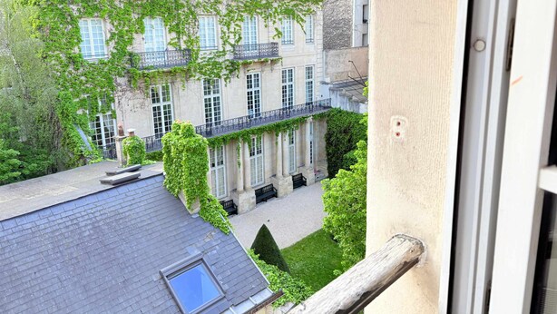 A courtyard with a building covered in ivy, a small garden, and a balcony with a window. - Heart Marais Bright 1BR by Melvane (Paris)