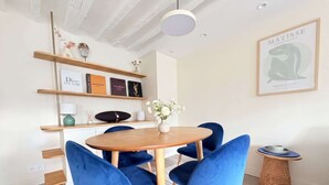 A dining area with a round wooden table, blue velvet chairs, a white rug, and a wall with framed items including a Matisse painting. - Heart Marais Bright 1BR by Melvane (Paris)