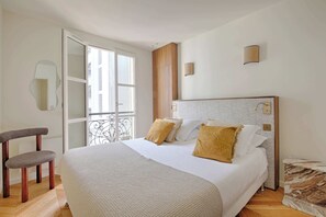 A bedroom with a bed, a chair, a window, and a wall-mounted light fixture. - Heart Marais Bright 2B, 6P, AC by Melvane (Paris)