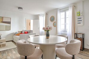 Ett modernt vardagsrum med ett runt matbord, beige stolar, en soffa med färgglada kuddar och en vas med blommor.