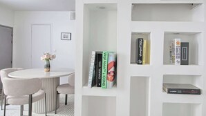 Ein modernes Zimmer mit einem runden Tisch, Stühlen, einem Bücherregal und einer Vase mit Blumen.