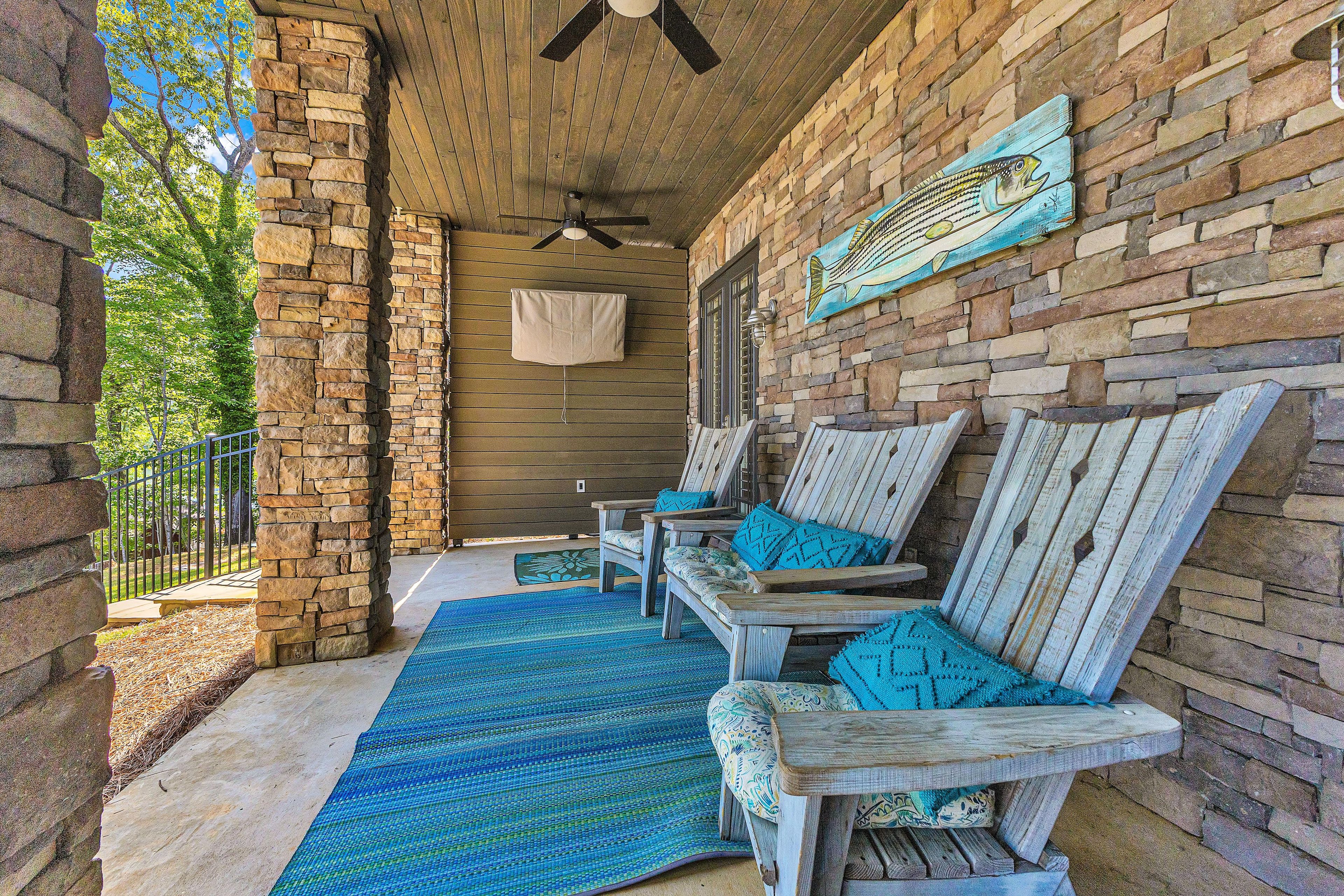 A covered porch with stone walls, wooden furniture, and a ceiling fan.